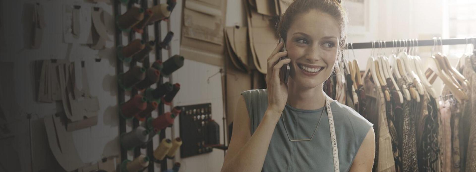 Une femme au téléphone devant un présentoir contenant des habits suspendus