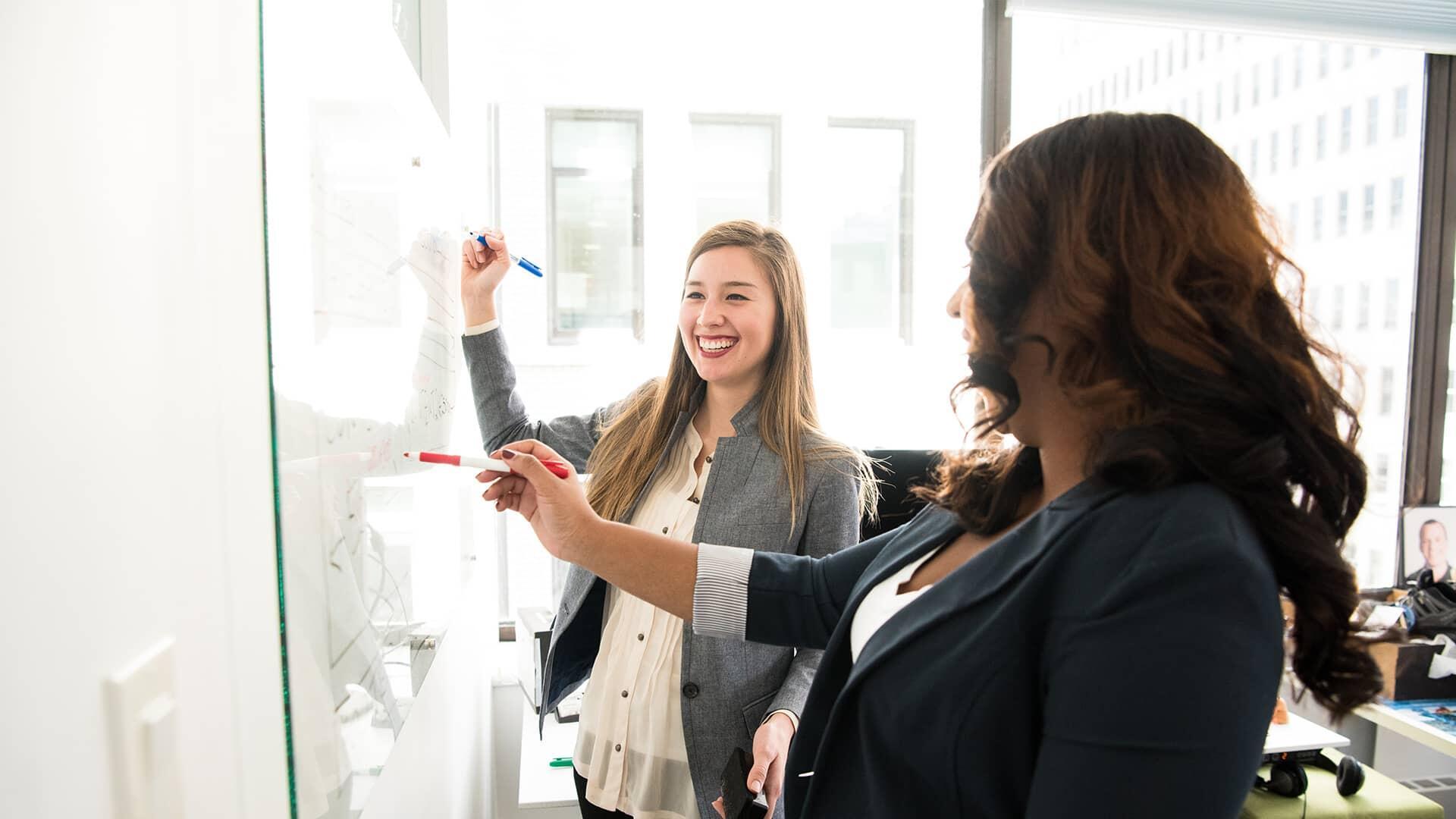 Deux femmes souriant devant un tableau blanc
