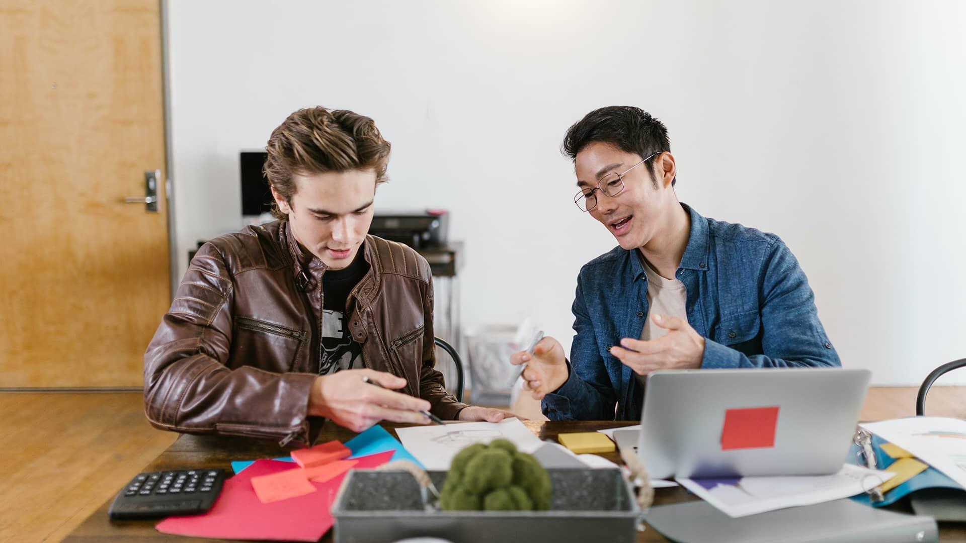Deux jeunes hommes derrière un bureau en train de regarder des papiers sur un burea