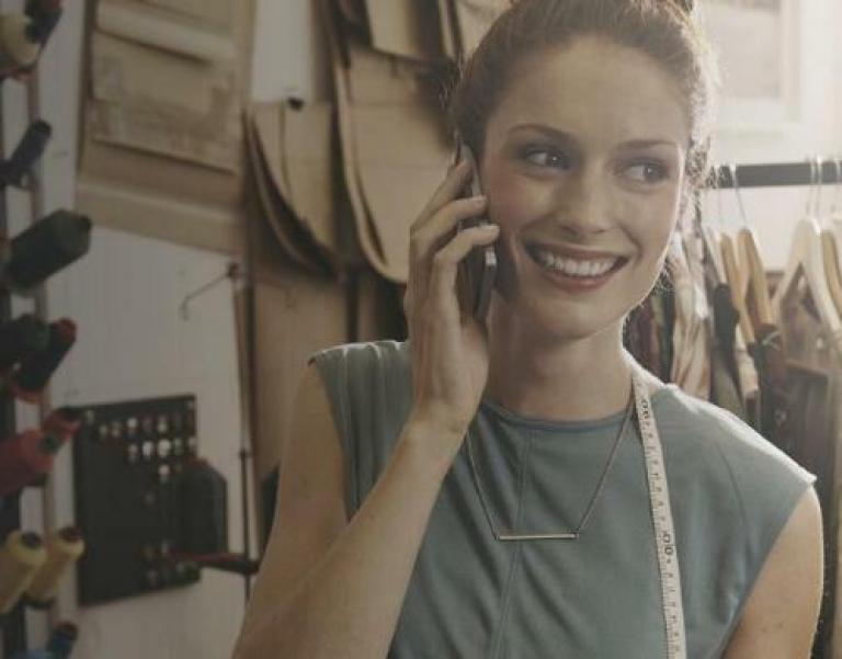 Une femme au téléphone devant un présentoir contenant des habits suspendus