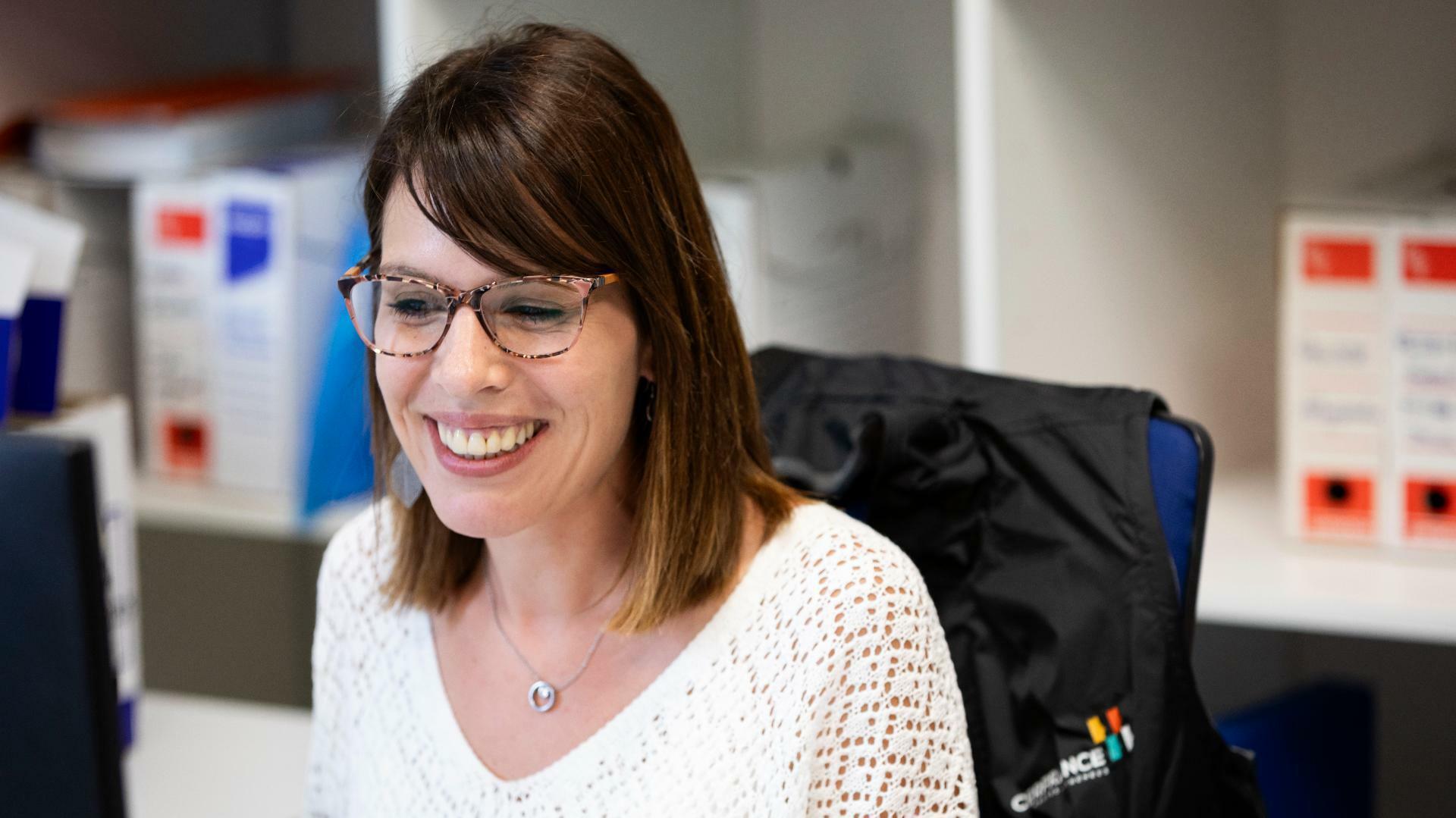 Expertise en management en ressources humaines, Cerfrance vous accompagne, une RH Cerfrance souriante devant son ordinateur avec une doudoune logoté sur sa chaise