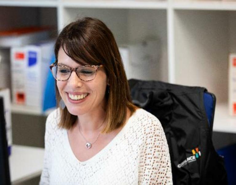 Expertise en management en ressources humaines, Cerfrance vous accompagne, une RH Cerfrance souriante devant son ordinateur avec une doudoune logoté sur sa chaise