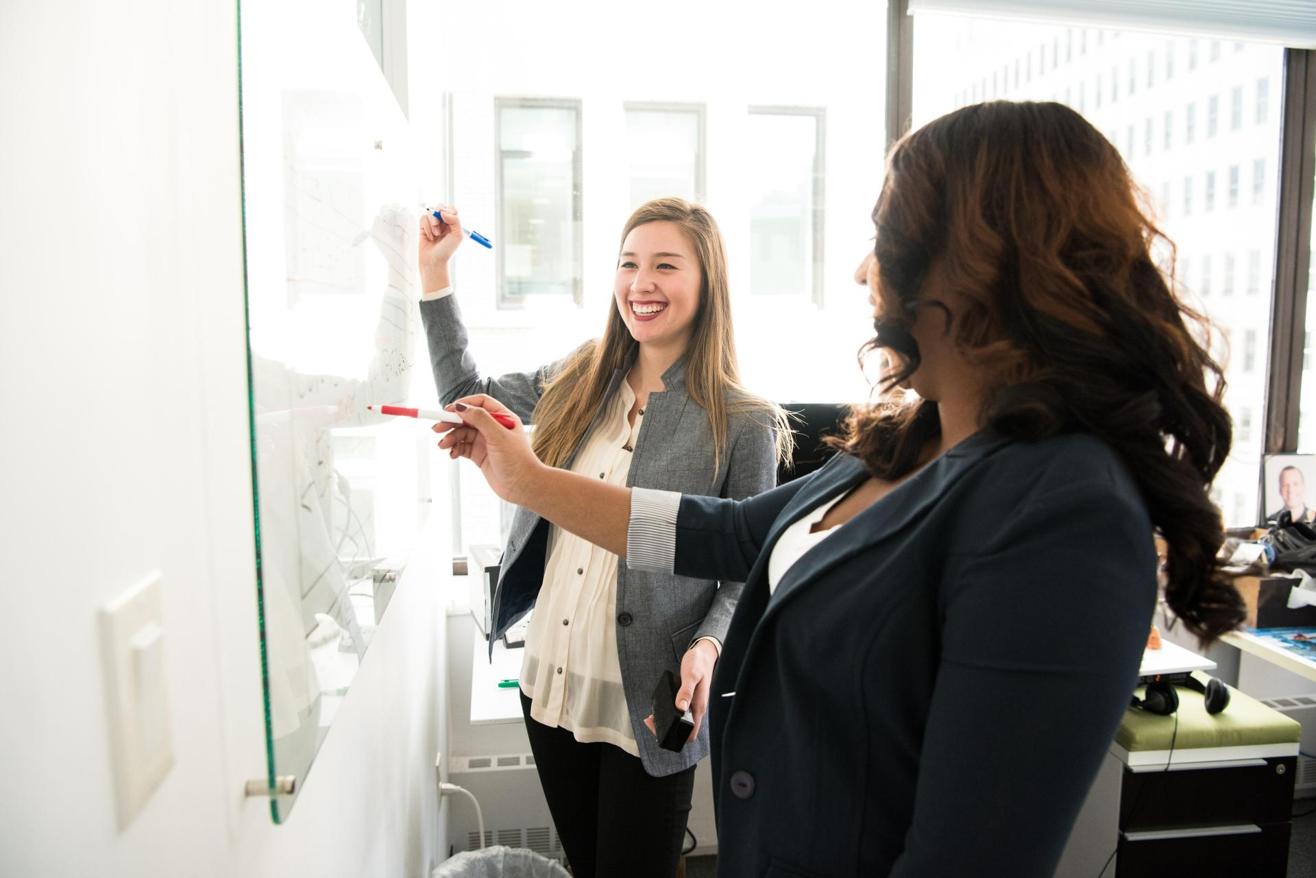 Deux femme dans une salle qui écrivent sur un tableau blanc, le conseil et la stratégie d'entreprise au cœur des débats