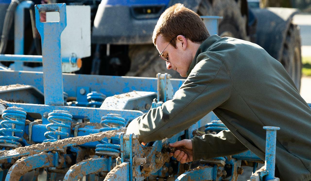 Un jeune agriculteur en train de réparer son tracteur